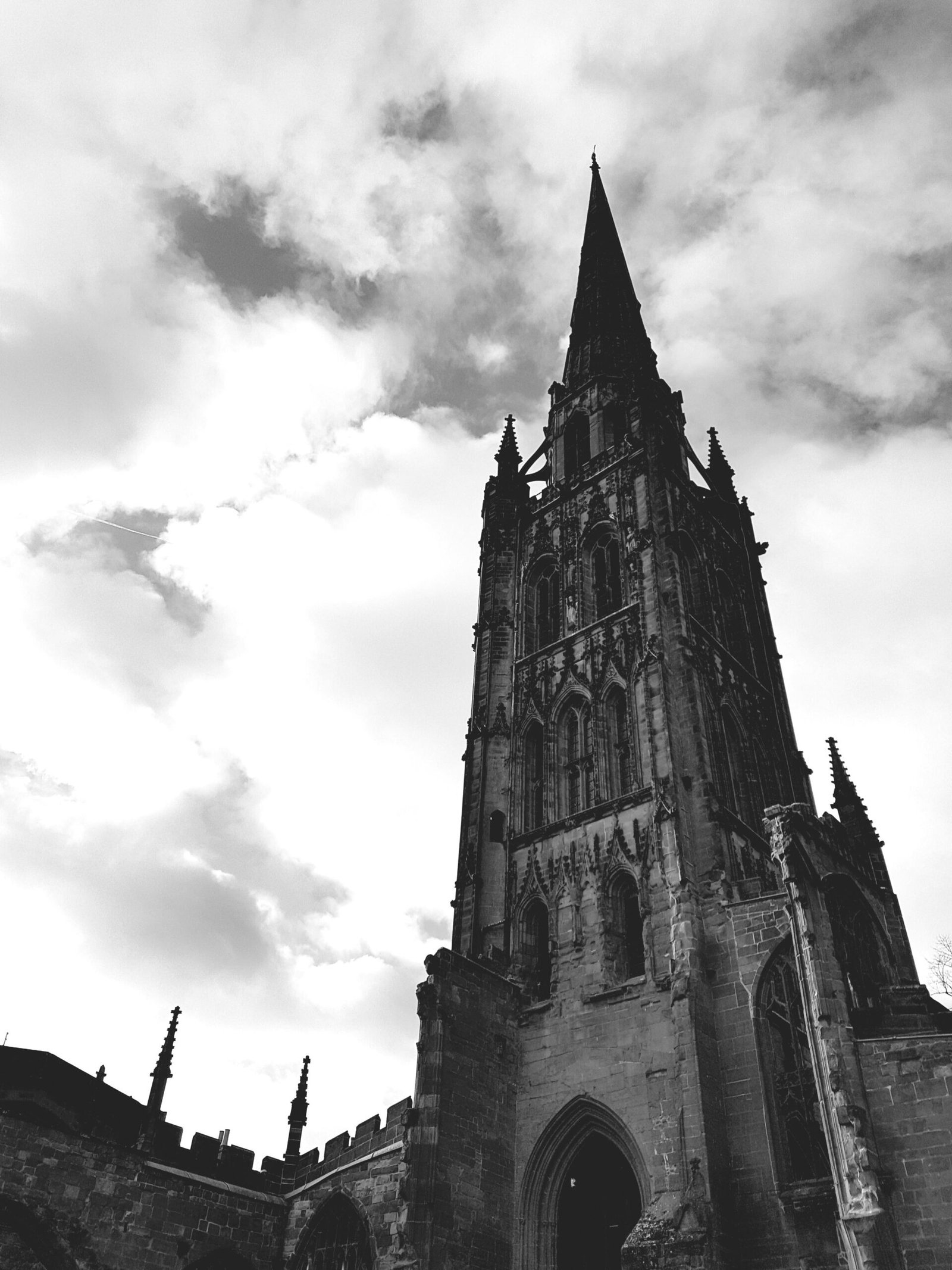 Monochrome view of a Gothic cathedral tower with dramatic cloudy sky backdrop.